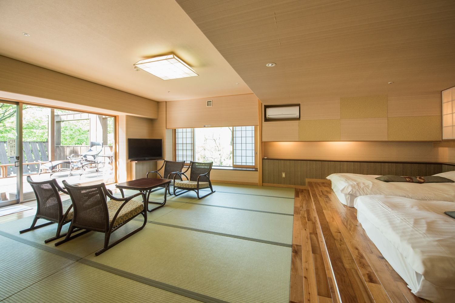 A hotel room with tatami flooring, a bed, a TV, and a seating area with chairs.