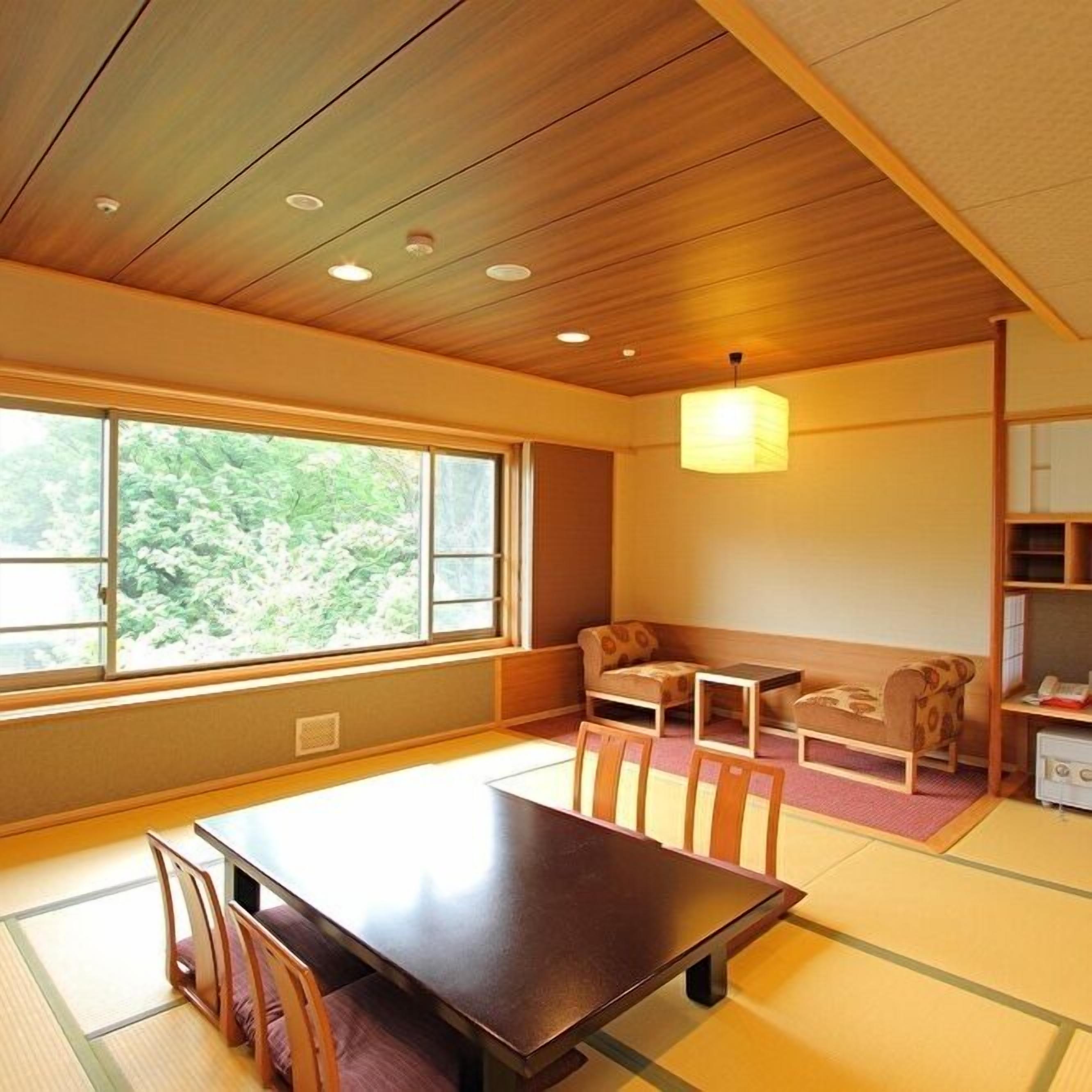 A traditional Japanese room with tatami flooring, a low table, chairs, a sofa, and a hanging light fixture.