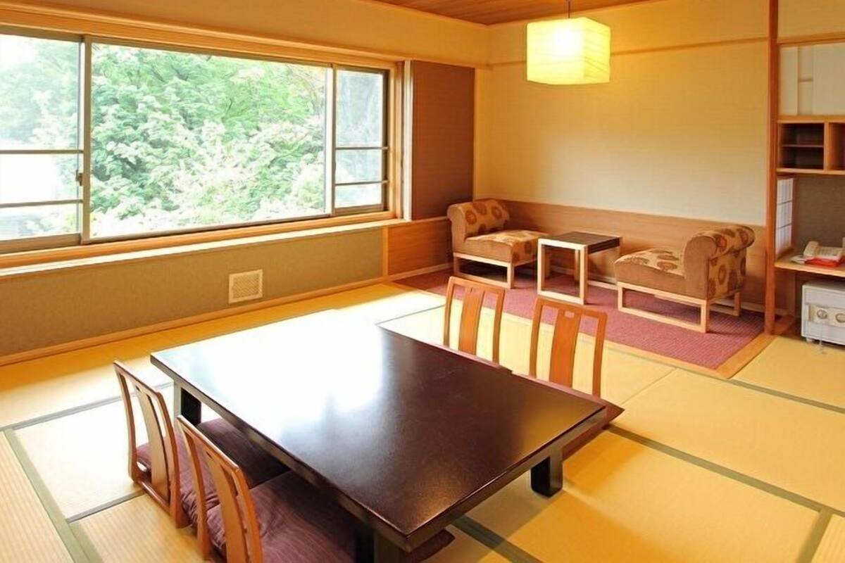 A traditional Japanese room with tatami flooring, a low table, chairs, a sofa, and a hanging light fixture.