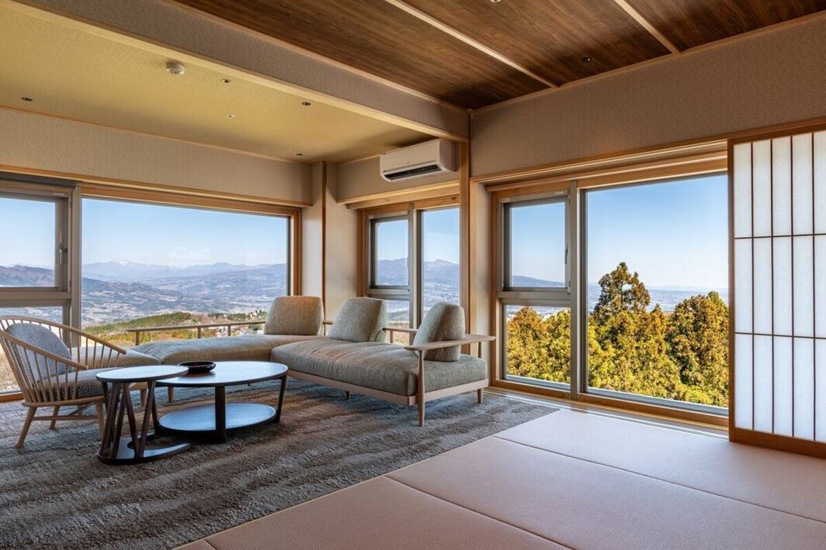 A room with a sofa, chairs, a table, and large windows offering a mountain view.