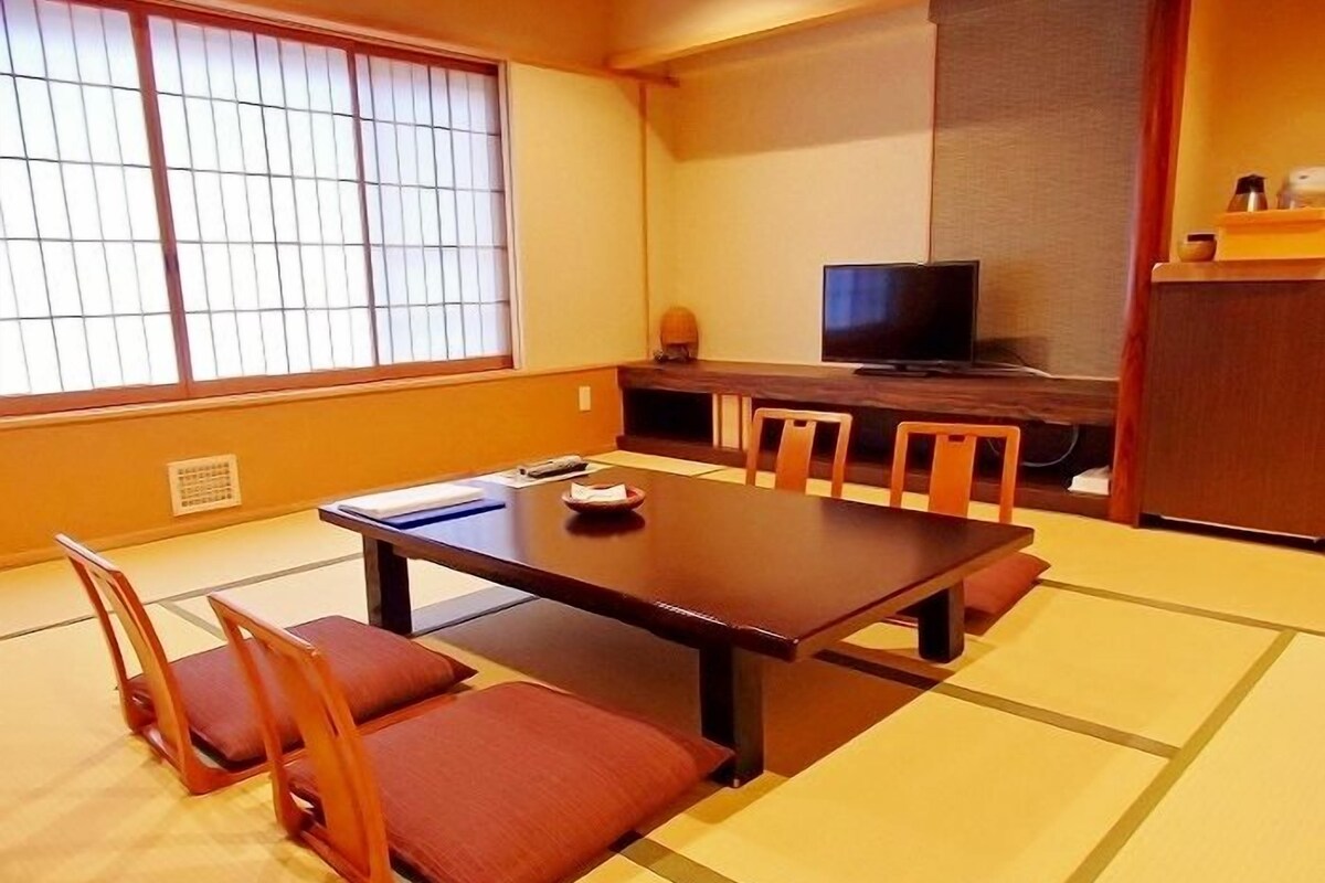 A traditional Japanese room with tatami flooring, a low table, and wooden chairs.