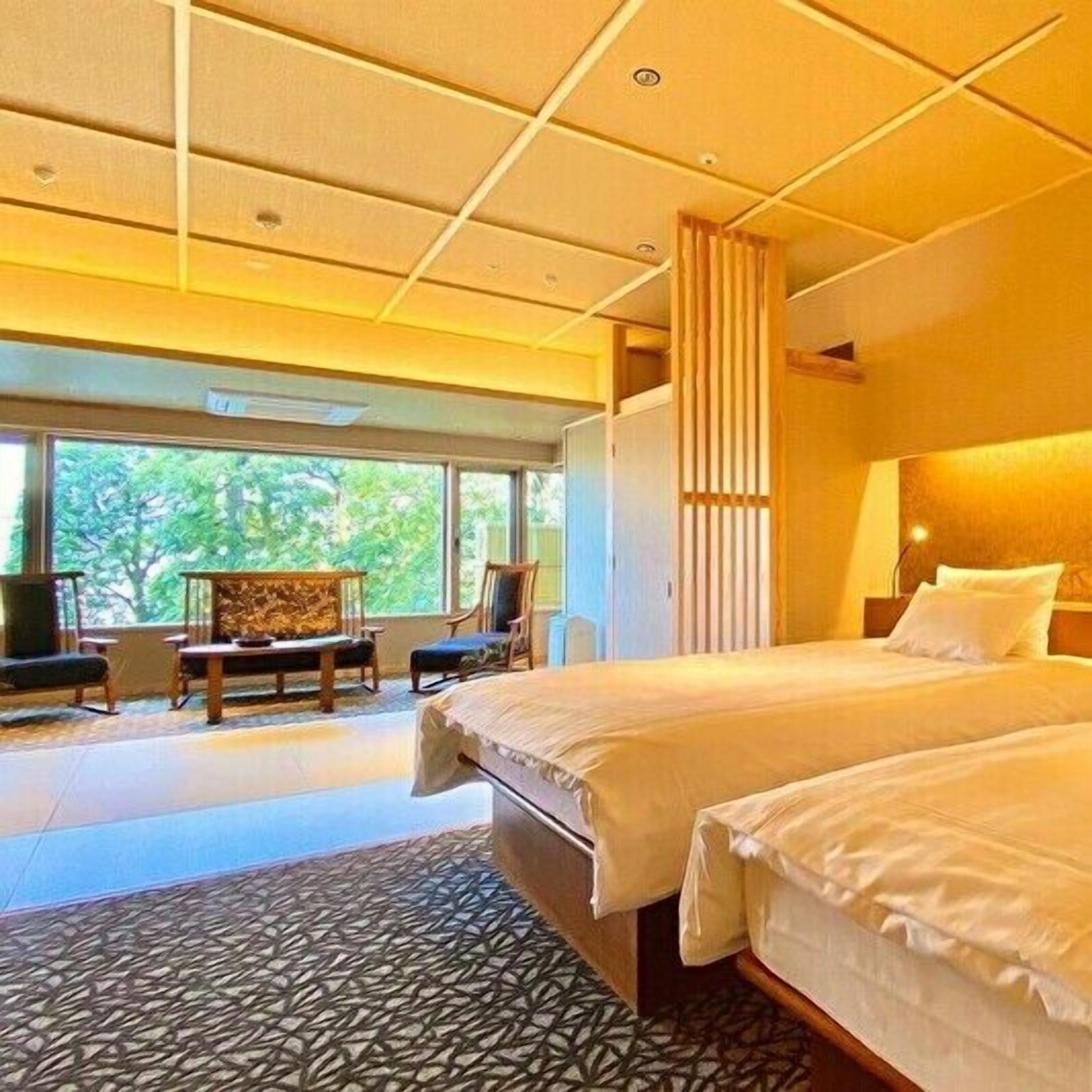 A hotel room with a large bed, a seating area with chairs, a view of greenery outside, and a patterned floor.