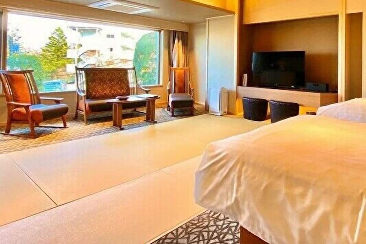 A hotel room with a bed, a TV, a seating area with chairs, and a large window.