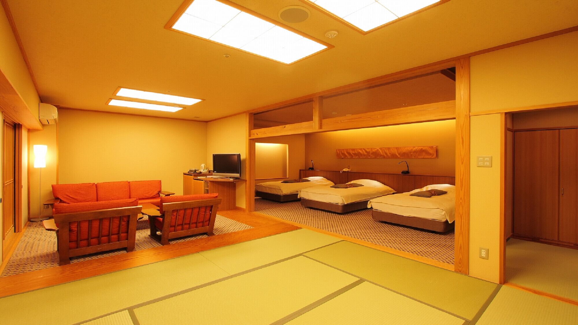 A traditional Japanese-style room with tatami flooring, a low wooden bed, a sofa, and a television.