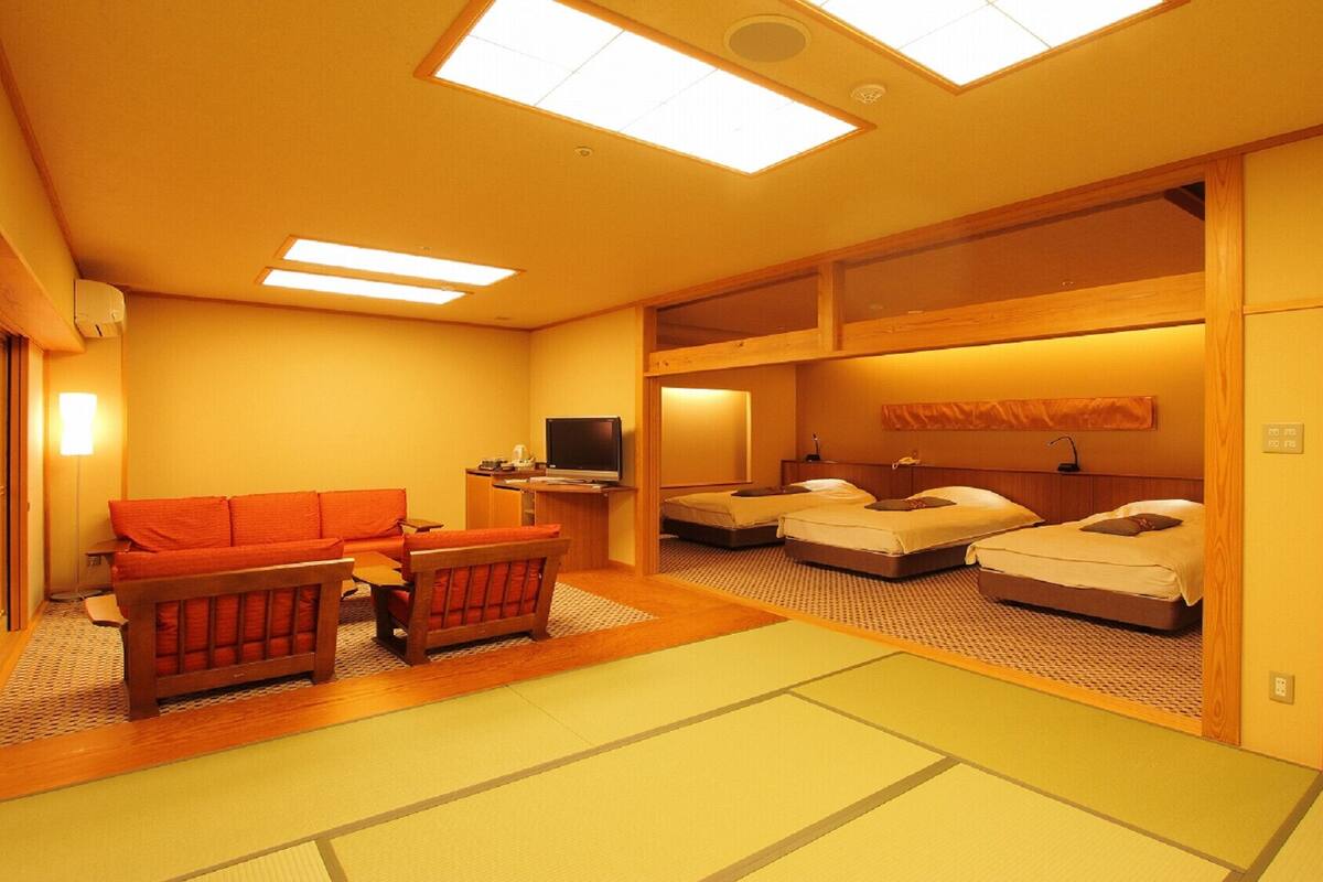 A traditional Japanese-style room with tatami flooring, a low wooden bed, a sofa, and a television.