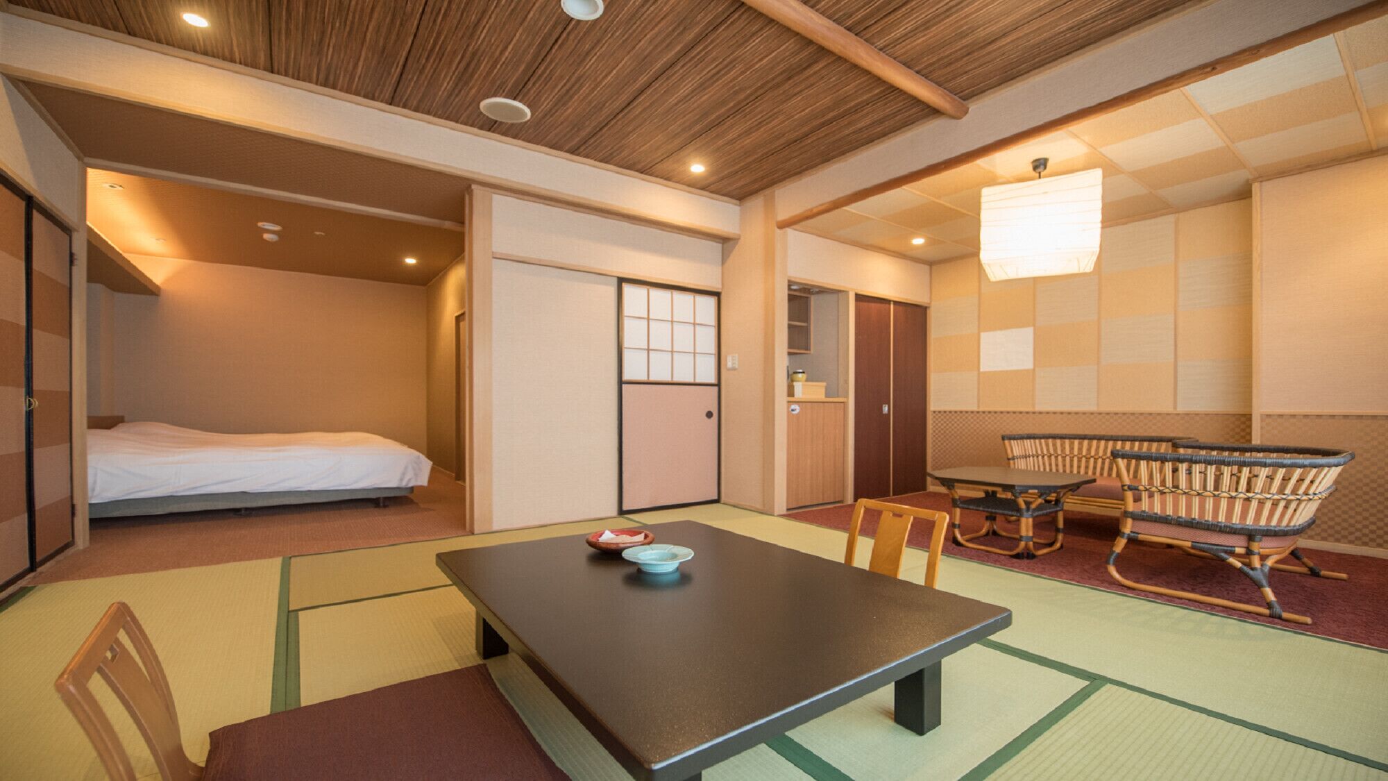 A traditional Japanese-style room with tatami flooring, a low table with a cushion, a futon bed, and a washbasin.