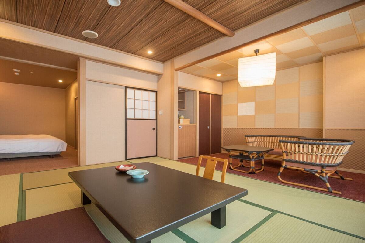 A traditional Japanese-style room with tatami flooring, a low table with a cushion, a futon bed, and a washbasin.