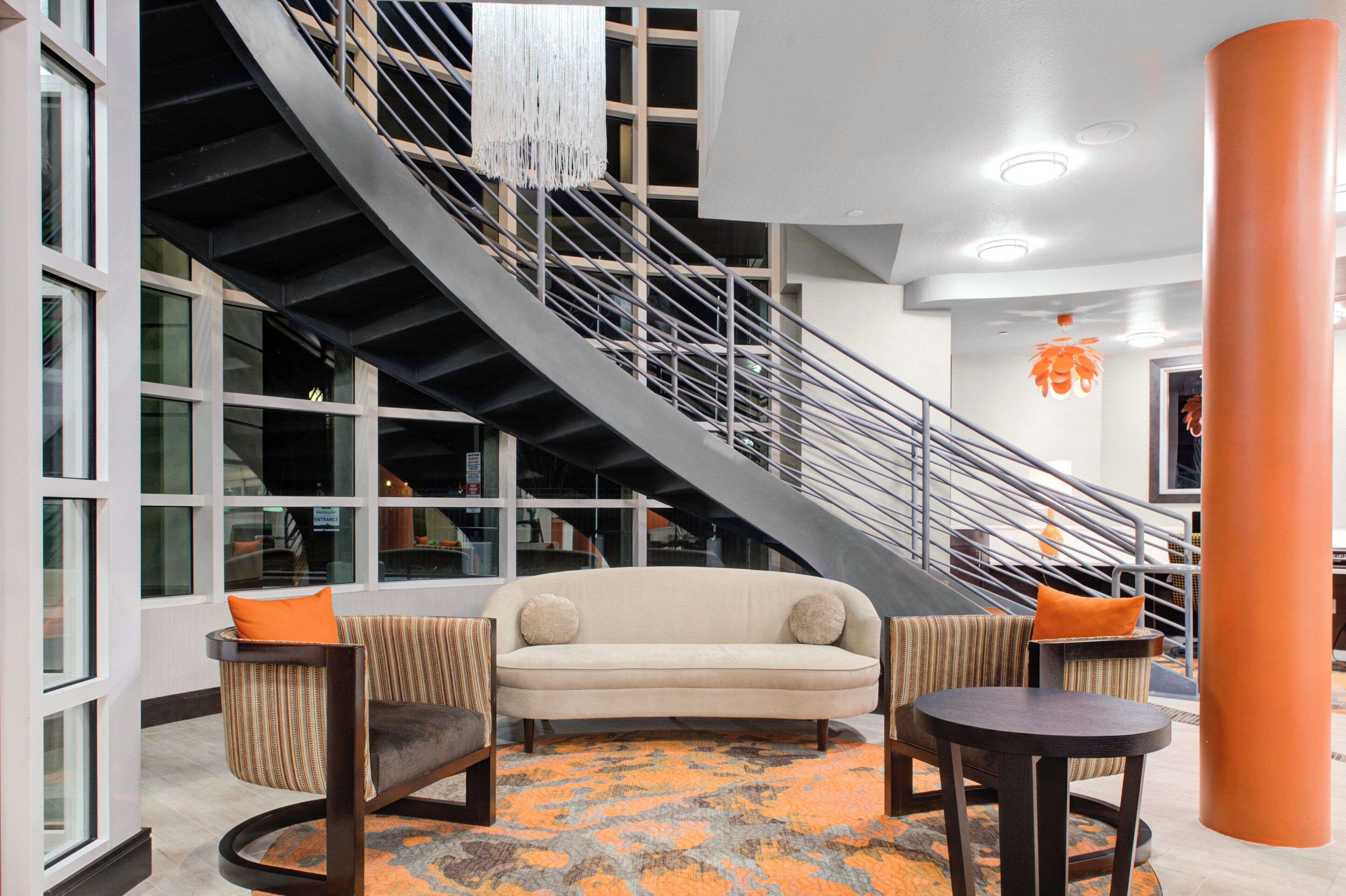 A modern interior with a spiral staircase, a beige sofa, two armchairs, and a patterned rug.