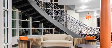 A modern interior with a spiral staircase, a beige sofa, two armchairs, and a patterned rug.