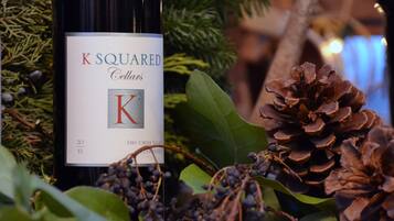 A bottle of K Squared Cellars wine with a label, surrounded by pine cones and greenery.