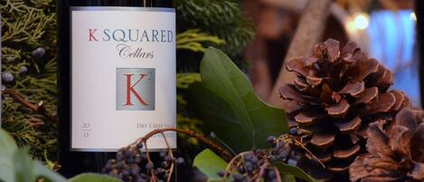 A bottle of K Squared Cellars wine with a label, surrounded by pine cones and greenery.