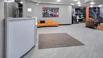 En moderne lobby med en reception, et siddeområde med en orange sofa, et mønstret tæppe og en trappe i baggrunden.
