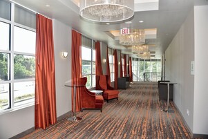 Un pasillo de hotel con alfombra estampada, asientos tapizados en rojo y amplias ventanas con cortinas.