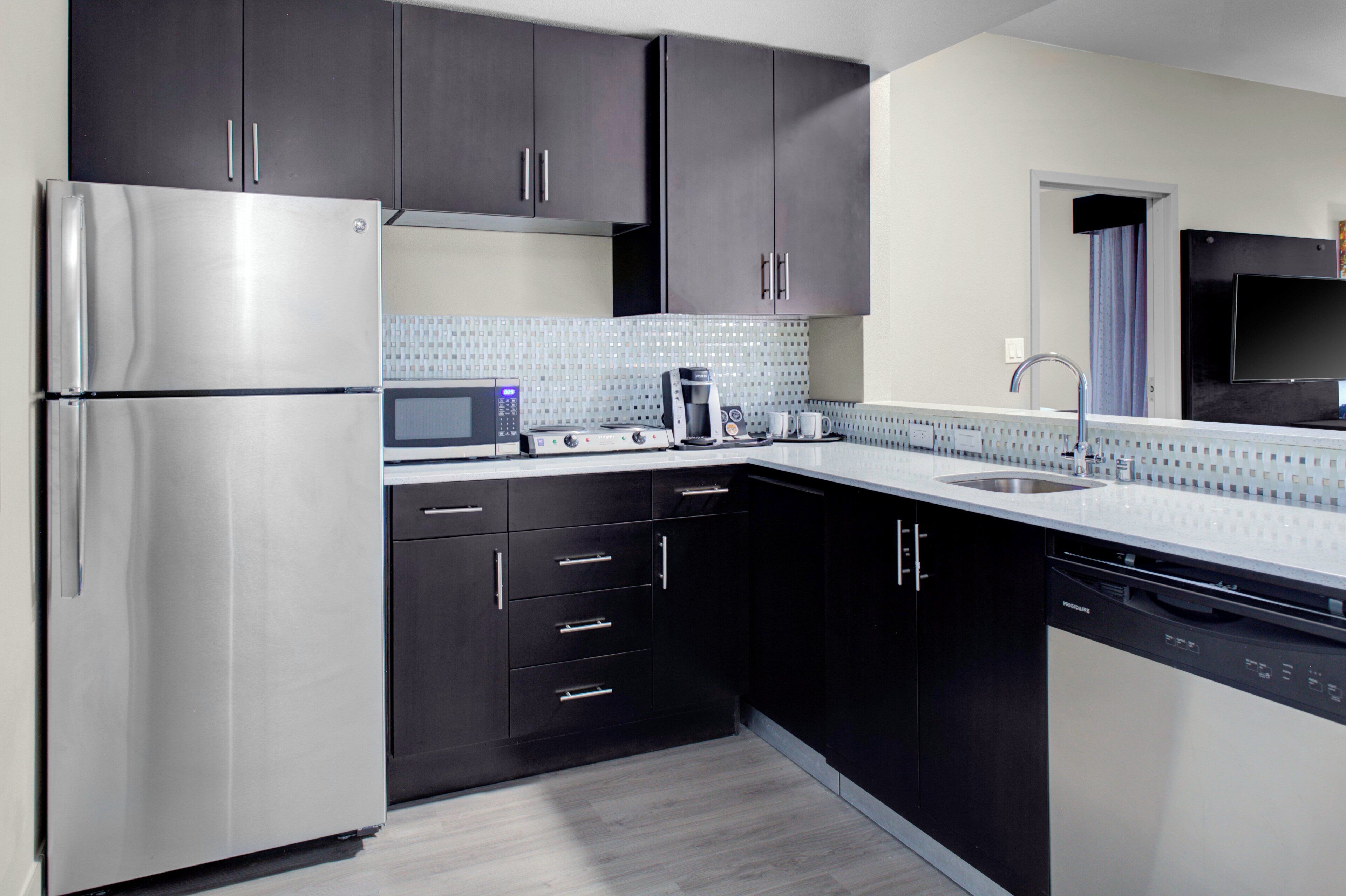 Una cocina moderna con armarios oscuros, electrodomésticos de acero inoxidable, microondas y lavavajillas.