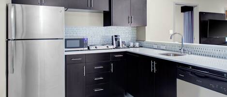 Una cocina moderna con armarios oscuros, electrodomésticos de acero inoxidable, microondas y lavavajillas.