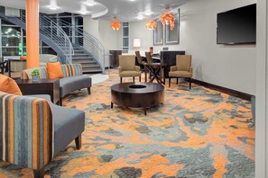 A hotel lobby with a spiral staircase, seating area with sofas and armchairs, a coffee table, and a flat-screen TV mounted on the wall. - Holiday Inn Windsor Wine Country by IHG (Windsor)