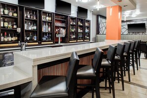 A bar area with a long counter, multiple shelves of bottles, and several bar stools. - Holiday Inn Windsor Wine Country by IHG (Windsor)