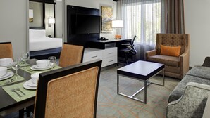 A hotel room with a bed, a TV, a desk, a chair, a table, and a dining area with a table set for two. - Holiday Inn Windsor Wine Country by IHG (Windsor)