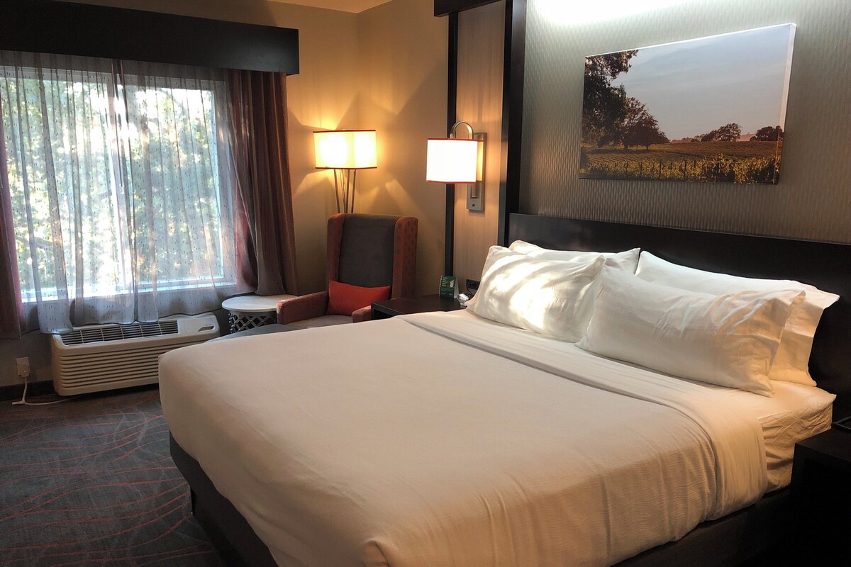 Een hotelkamer met een groot bed, een stoel, een tafel en een wandlamp.