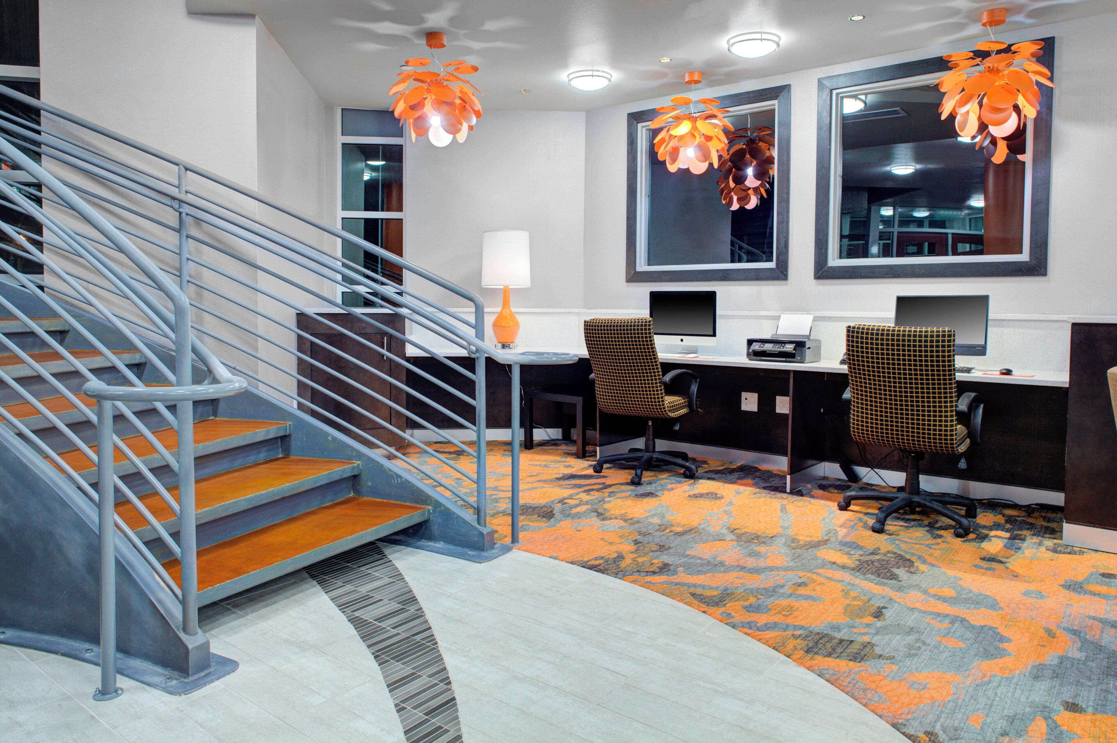Un espace de bureau moderne comprenant un escalier, des bureaux, des chaises et une moquette à motifs.