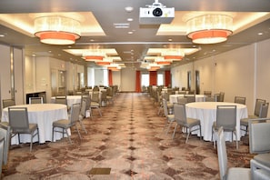 A conference room with multiple tables and chairs, a carpeted floor, and ceiling-mounted lighting fixtures.