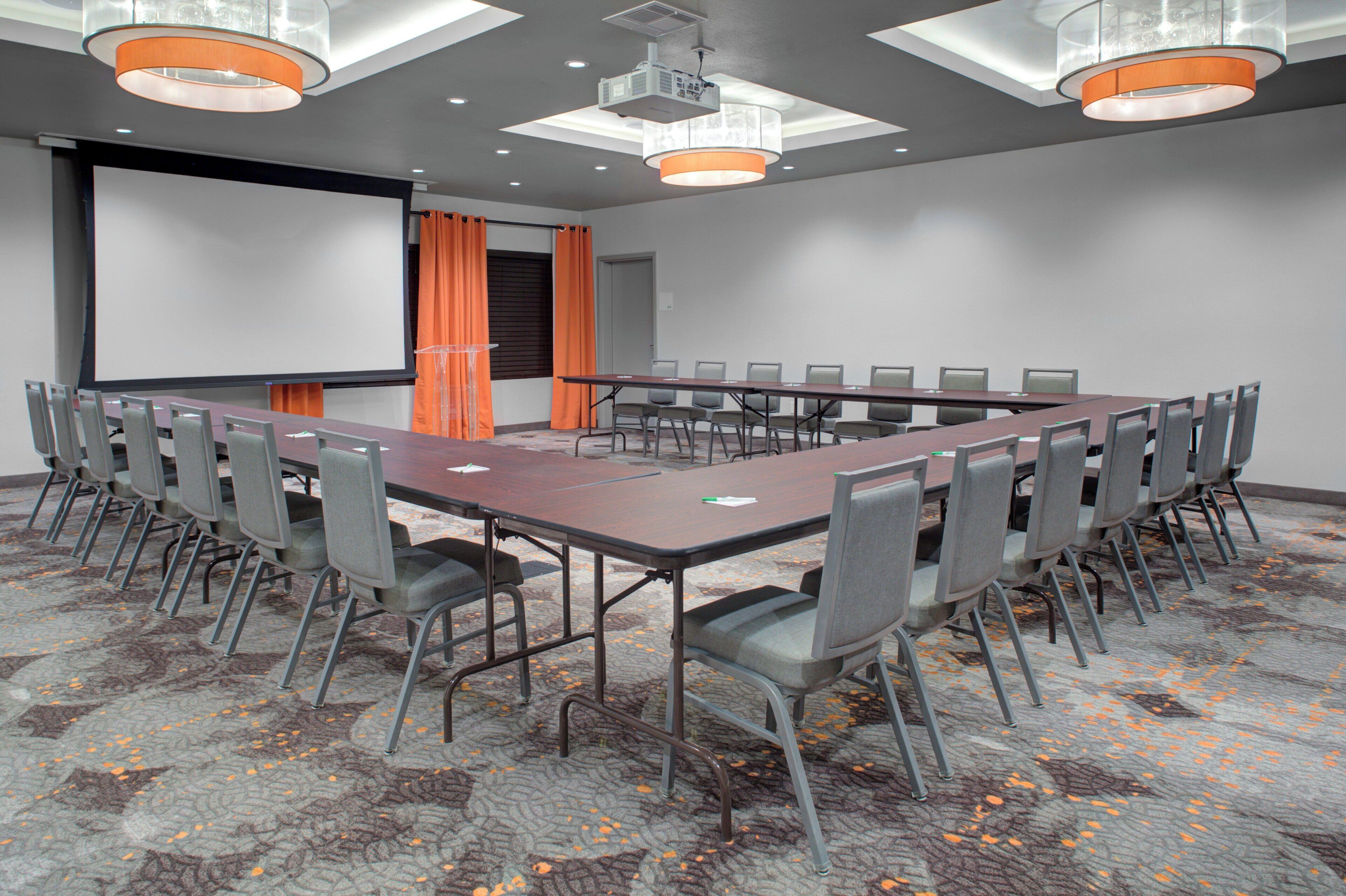A conference room with a long table, chairs, a projector screen, and a presentation podium.