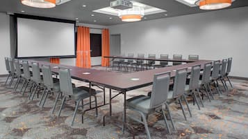 A conference room with a long table, chairs, a projector screen, and a presentation podium.