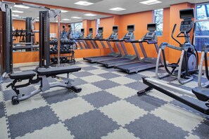 Ein Fitnessstudio mit Laufbändern, Kraftgeräten und einer Spiegelwand.