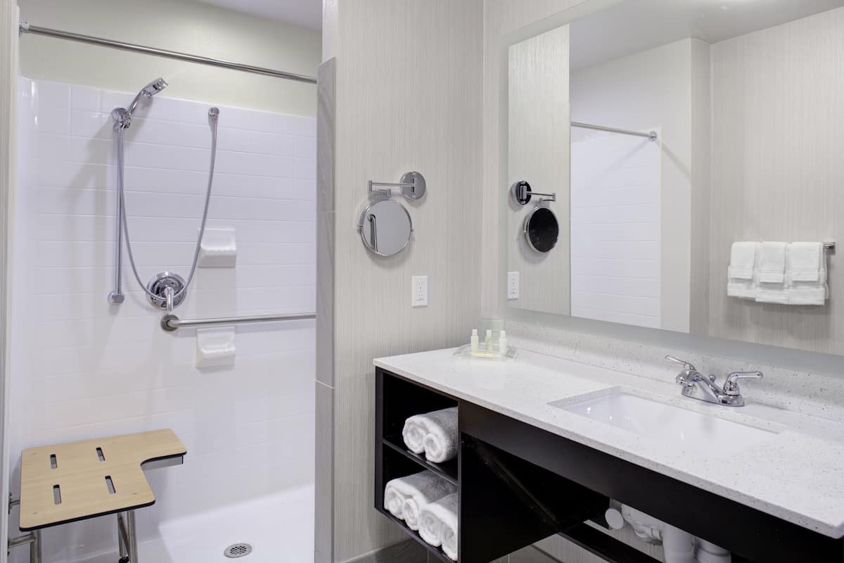 Un baño moderno con bañera, ducha y lavamanos. Hay un perchero, un espejo y un estante con toallas.