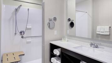 Un baño moderno con bañera, ducha y lavamanos. Hay un perchero, un espejo y un estante con toallas.
