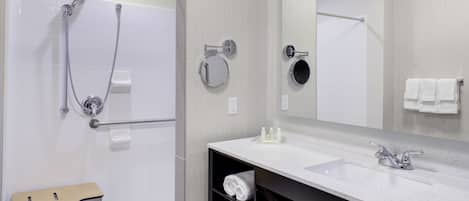 A modern bathroom with a bathtub, shower, and sink. There is a towel rack, a mirror, and a shelf with towels.