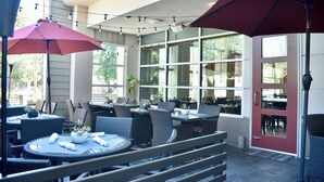 An outdoor patio area with round tables and chairs, umbrellas, and potted plants. - Holiday Inn Windsor Wine Country by IHG (Windsor)