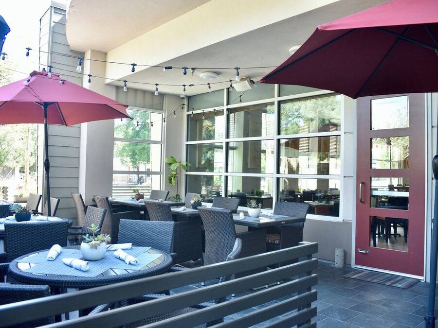 Un espace extérieur aménagé en terrasse, avec des tables et des chaises rondes, des parasols et des plantes en pot.