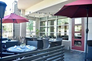 An outdoor patio area with round tables and chairs, umbrellas, and potted plants.