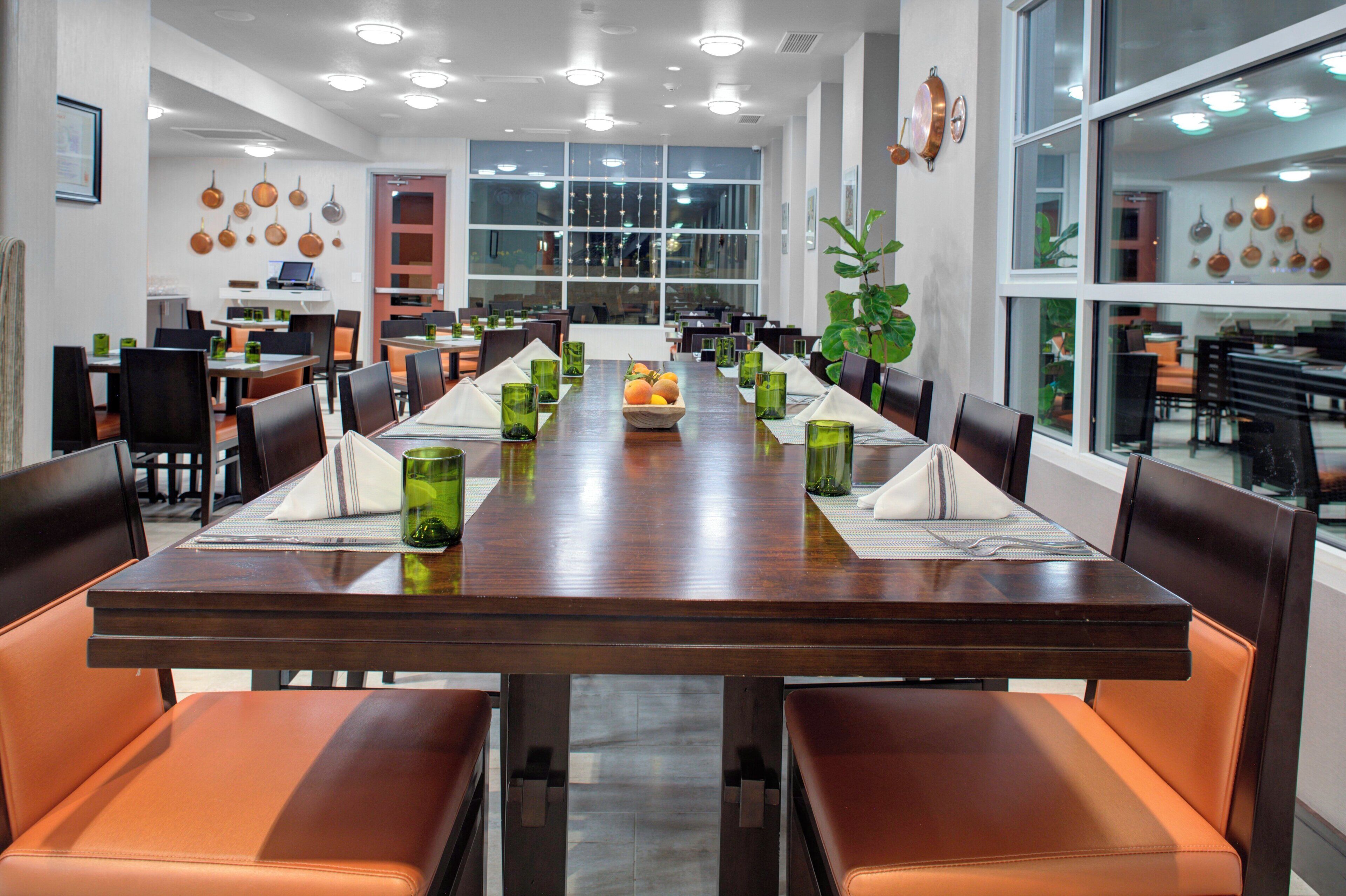 A long dining table with chairs, green glassware, and a fruit basket.