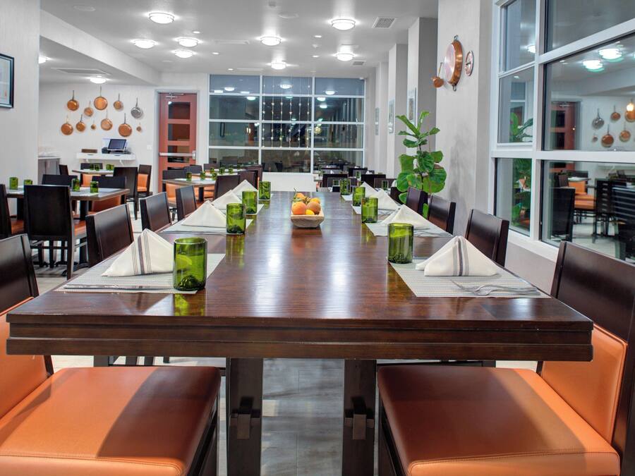 A long dining table with chairs, green glassware, and a fruit basket.