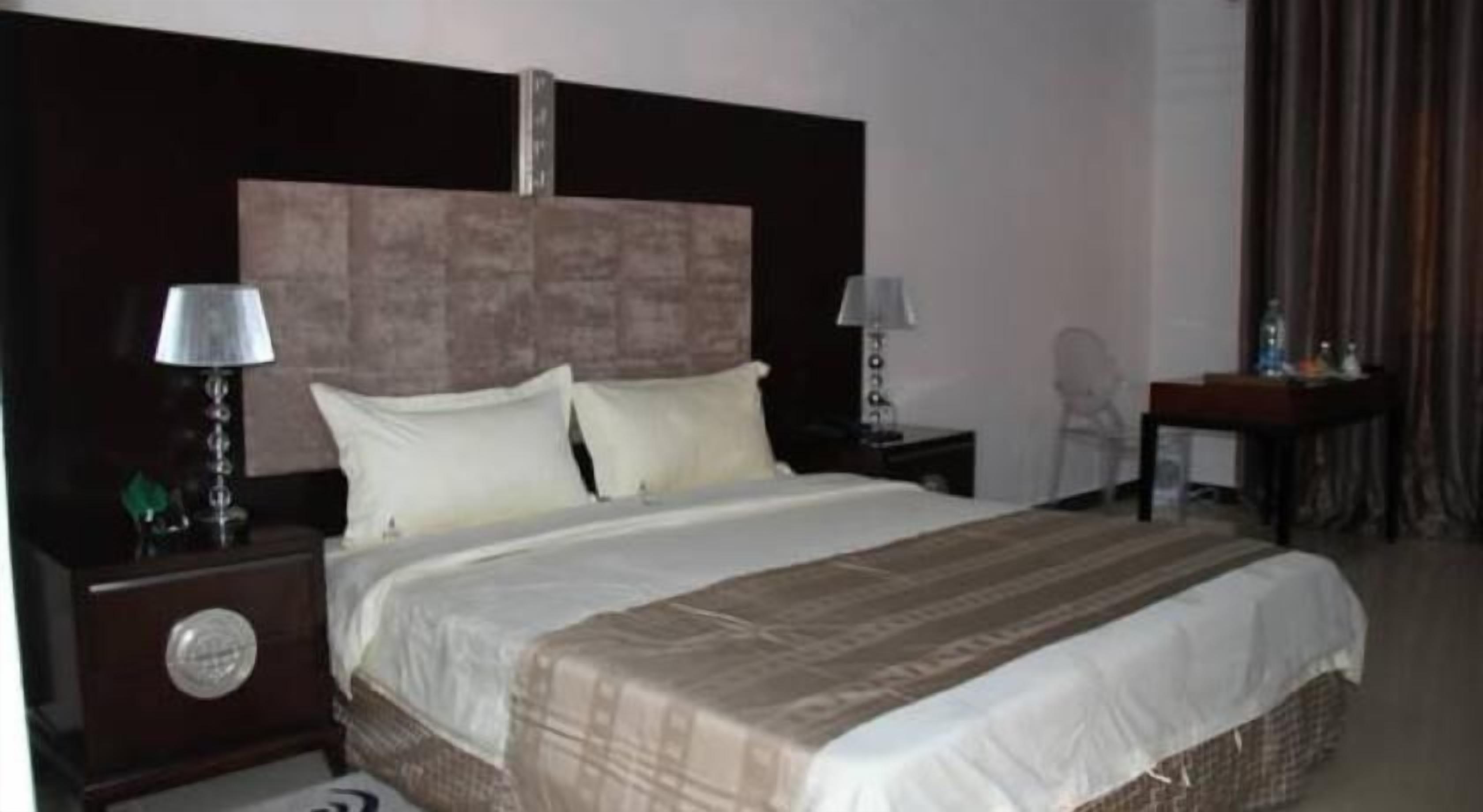 Une chambre d’hôtel avec un grand lit, deux tables de chevet avec des lampes, une tête de lit en bois et un petit bureau avec une chaise.