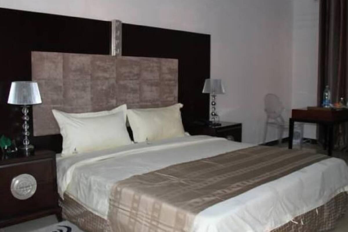 Une chambre d’hôtel avec un grand lit, deux tables de chevet avec des lampes, une tête de lit en bois et un petit bureau avec une chaise.