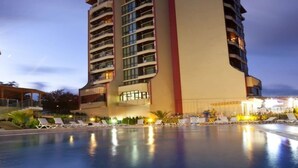 Un hotel de varios pisos con un área de piscina, que incluye tumbonas y una piscina bien iluminada.