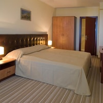 Una habitación de hotel con una cama grande, un armario de madera, una puerta y una mesita de noche con una lámpara.