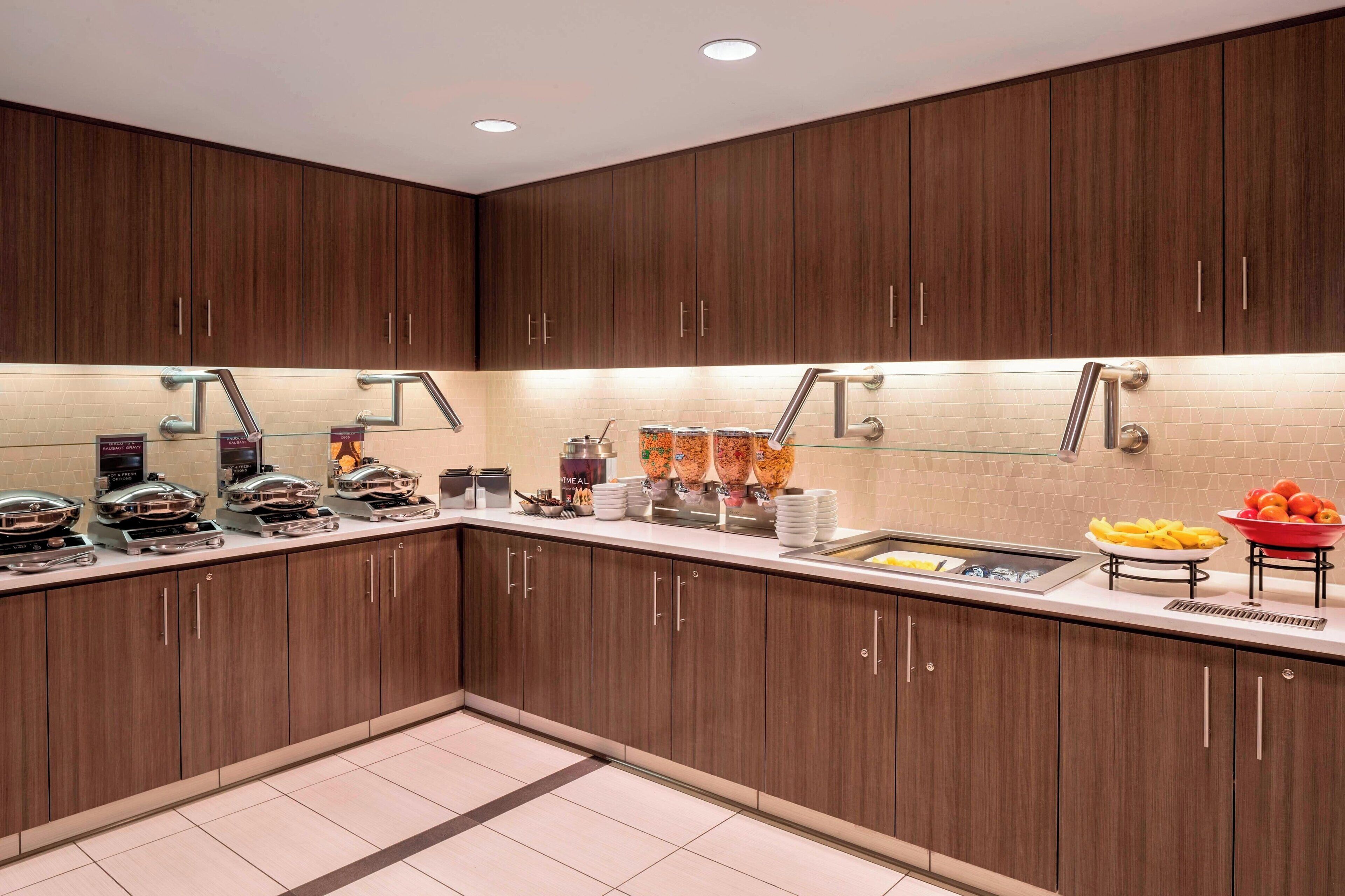 A modern kitchen with wooden cabinets, stainless steel appliances, and a variety of food items on the counter.
