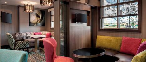 Una habitación de hotel moderna con sofá, sillas, una mesa de comedor y televisor.