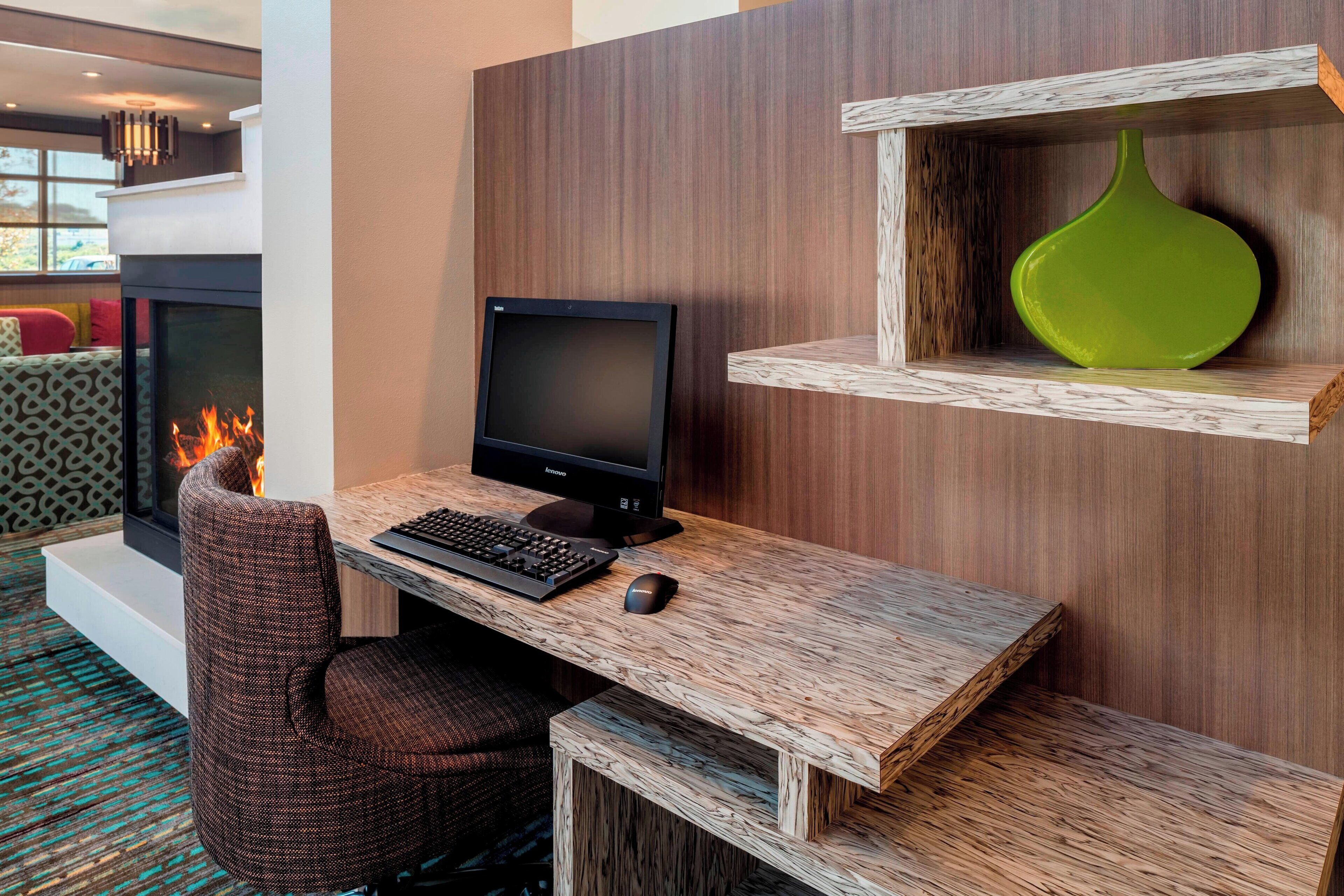A modern room with a fireplace, a computer desk, and a green vase on a shelf.