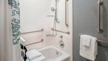 A bathroom with a bathtub, a shower with grab bars, a towel rack, and a toilet with a grab bar.