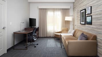 Quarto de hotel com escrivaninha, cadeira, sofá e televisão.