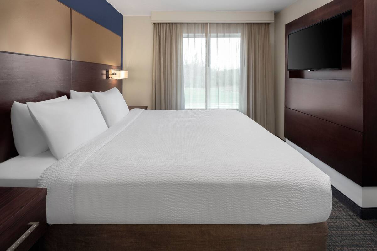 Een hotelkamer met een groot bed, een flatscreen televisie aan de wand en een raam met gordijnen.