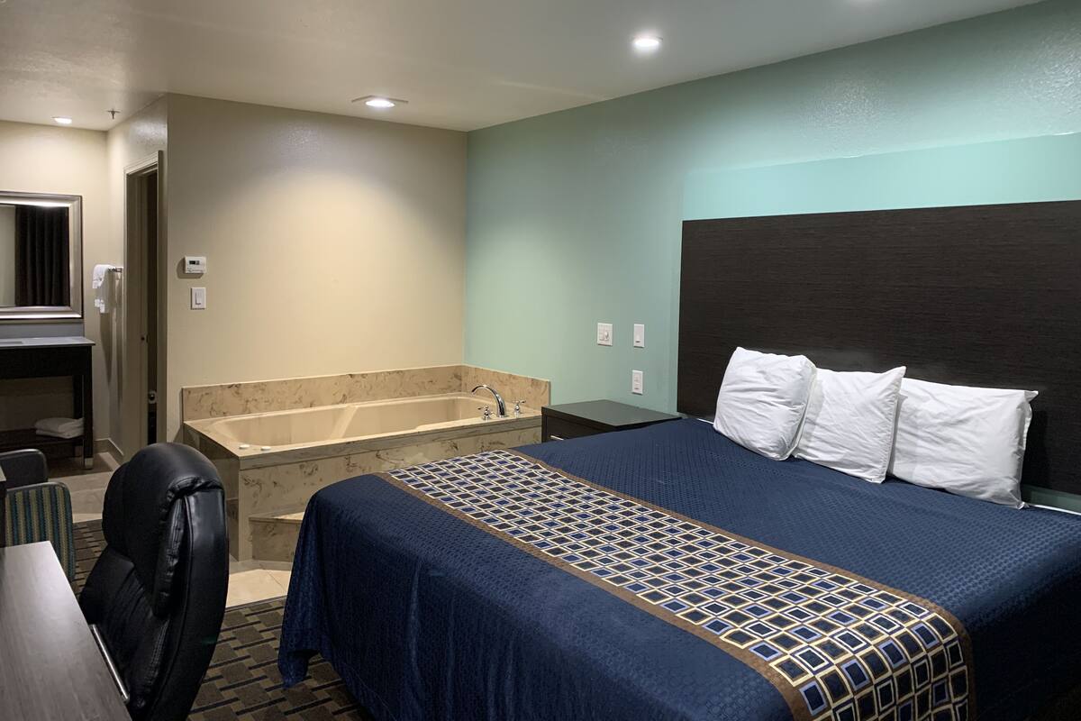 A hotel room with a large bed, a separate bathroom with a bathtub, a desk, and a chair.