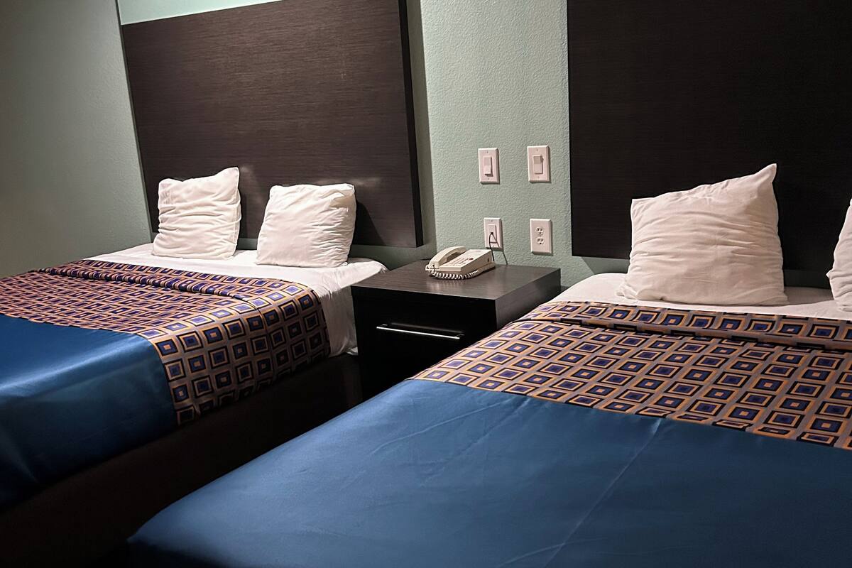 A hotel room with two beds, each with patterned bedding, a bedside table with a phone, and a wall-mounted light.