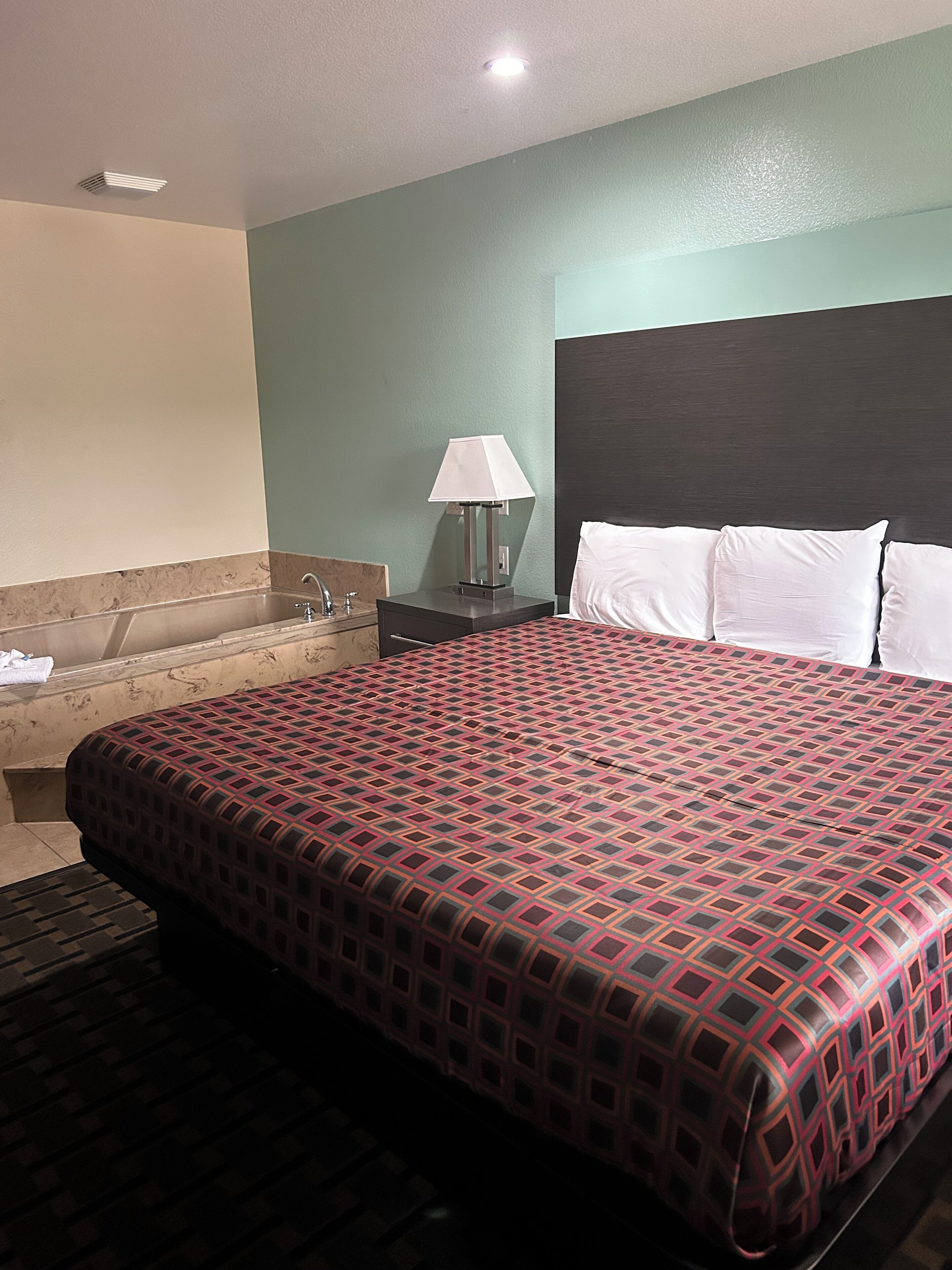 Een hotelkamer met een groot bed, een nachtkastje, een lamp en een bad.