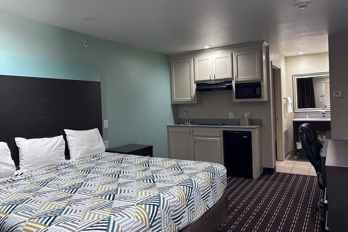 A hotel room with a bed, a small kitchenette, a bathroom, and a desk.